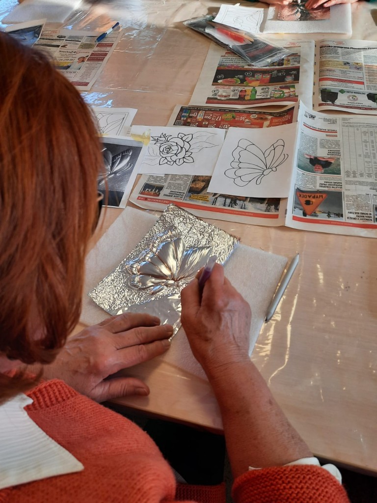 Jedna z uczestniczek warsztatów wykonująca pracę plastyczną - srebrną płaskorzeźbę przedstawiającą motyla.