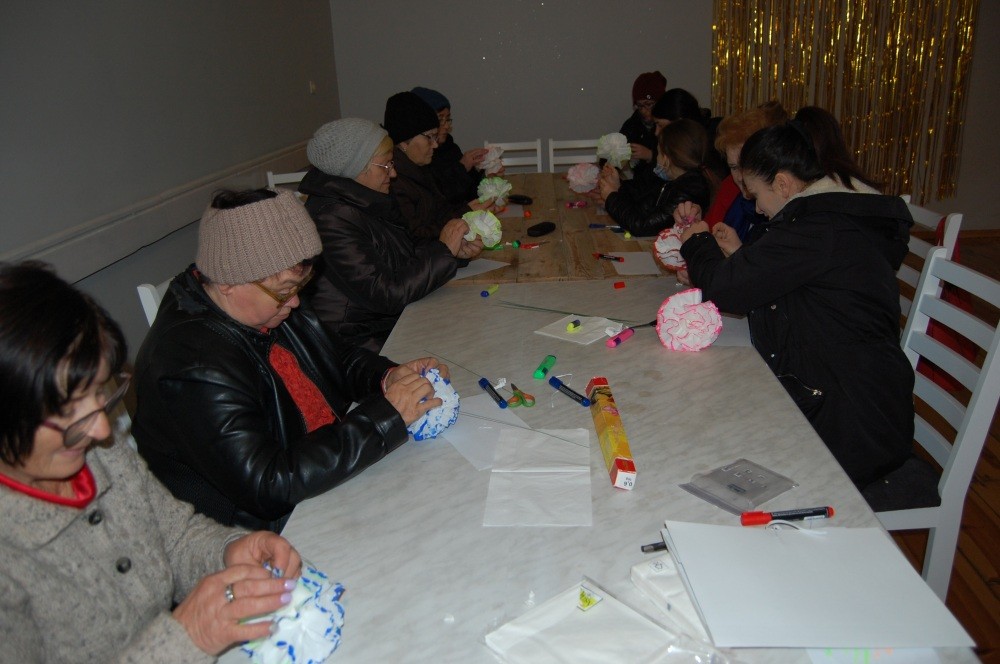 Zbliżenie na uczestników zajęć, którzy tworzą papierowe kwiaty przy stole.
