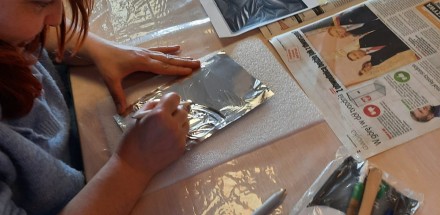 Uczestniczka siedząca przy stole w trakcie tworzenia srebrnej płaskorzeźby.