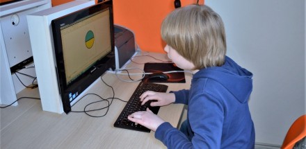 Zbliżenie na chłopca, który siedzi przed komputerem i wykonuje pracę w programie graficznym.