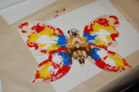 Pomalowany, drewniany motyl w kolorach żółto-czerwono-niebiesko-brązowych.