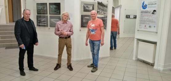 Dwóch mężczyzn stoją przed wystawą fotografii. Jeden z nich ubrany jest elegancko, drugi w koszulkę i jeansy.