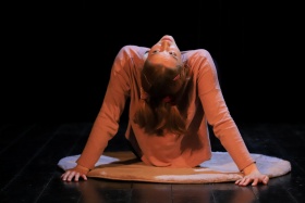 Występ sceniczny, kobieta siedząca na dywanie, z głową podniesioną do góry.