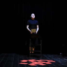 Występ sceniczny. Kobieta stojąca na scenie, przed nią rozłożone czerwone kartki na podłodze.