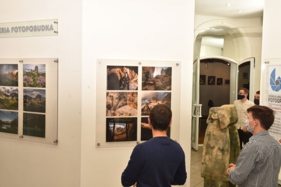 Ludzie obserwujący wystawę fotografii. Na ścianach są zamieszczone zdjęcia w kolaże.