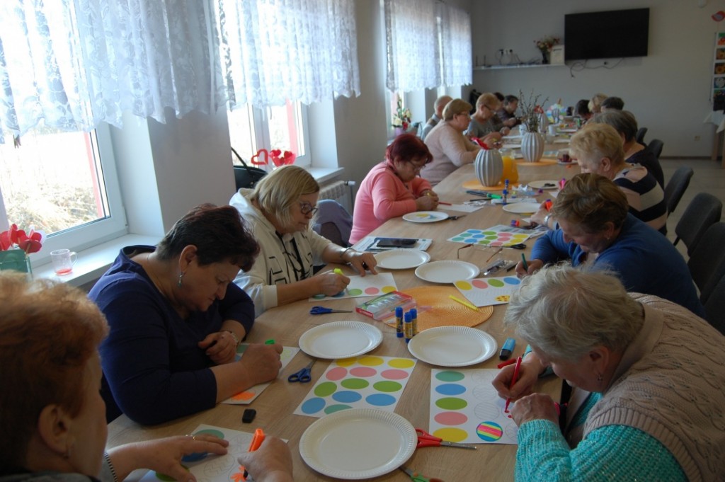 Uczestnicy zajęć plastycznych siedzą przy stole i tworzą prace - kolorowe jajka wielkanocne z papieru.
