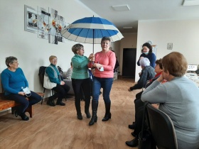 Uczestniczki warsztatów teatralnych stoją na korytarzu - dwie z nich trzyma biało-niebieski parasol.