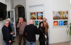 Grupa osób stojąca na sali wystaw. Mężczyzna rozmawia przez telefon. Na ścianie wiszą obrazy.
