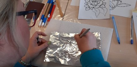 Zbliżenie na uczestniczkę warsztatów, która tworzy pracę - srebrną płaskorzeźbę w formie kwiatu róży.