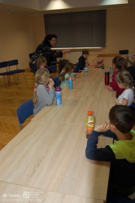 Dzieci siedzą przy stole w trakcie warsztatów teatralnych.