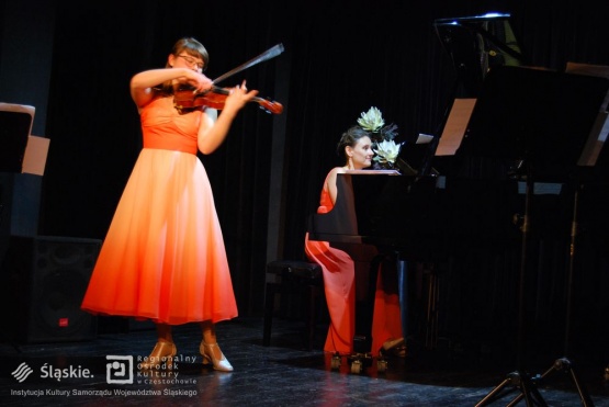 Kobieta gra na skrzypcach na scenie, w tle na pianinie gra inna artystka.
