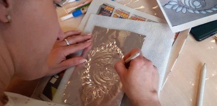 Uczestniczka warsztatów w trakcie tworzenia pracy plastycznej - srebrna płaskorzeźba przedstawiająca muszle.