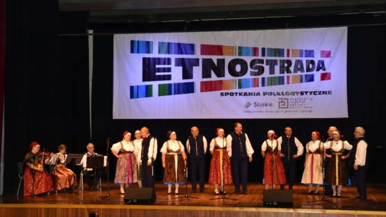 Grupa ludzi ubrana w strojach ludowych śpiewająca na scenie. W tle napis Etnostrada.