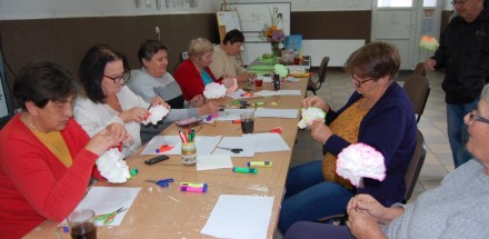 Panorama stołu przy którym siedzą uczestniczki warsztatów plastycznych, wykonujące prace - kolorowe kwiaty z papieru.