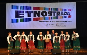 Kobiety w czerwono-biało i zielono-białych strojach ludowych stoją na scenie. W tle banner Etnostrada.