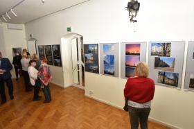 Kobieta przygląda się fotografii, które wiszą na ścianie. Fotografie przedstawiają Jurę Krakowsko-Częstochowską w różnych ujęciach.