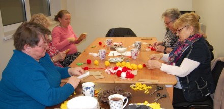 Uczestnicy zajęć siedzą przy stole i tworzą kolorowe ozdoby.