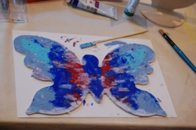 Pomalowany drewniany motyl w kolorach niebieskich i czerwonych.