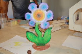 Praca plastyczna - drewniany kwiat pomalowany farbami, stojący na stole.