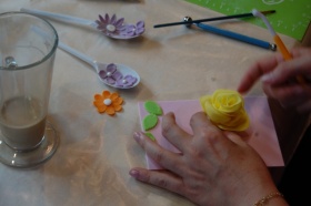 Proces tworzenia dekoracji kwiecistych. Osoba przykleja żółtą różę do różowej kartki.