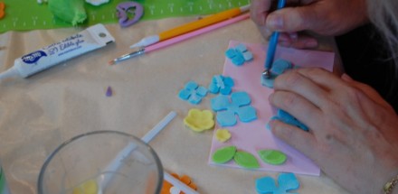 Uczestnik warsztatu wykonujący pracę plastyczną - niebieskie kwiaty.