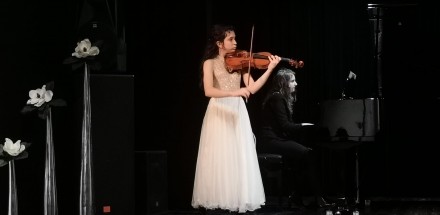 Kobieta gra na skrzypcach na scenie.