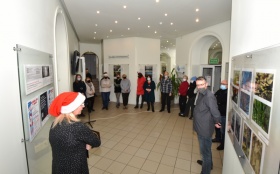 Grupa ludzi na sali, w tle widoczne fotografie. Kobieta nosi czapkę św. Mikołaja.