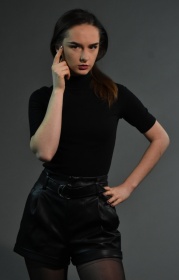 Sesja zdjęciowa w studio - kobieta ustawiona przodem, ubrana na czarno. Jedna ręka oparta na twarzy, druga ręka oparta na biodrze.