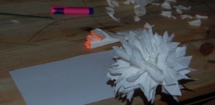 Zbliżenie na biały kwiat wykonany z papieru, który leży na stole. W tle widać różowy marker.