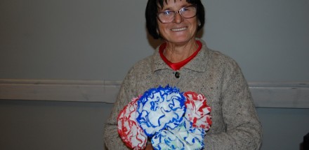 Jedna z uczestniczek zajęć prezentuje swoją prace - biało-niebieskie i biało-czerwone kwiaty wykonane z papieru.