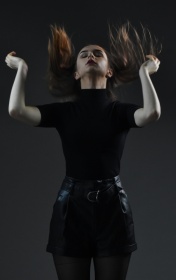 Kobieta ubrana na czarno pozuje do zdjęcia, ręce uniesione w górze, uchwycony moment poprawiania włosów.