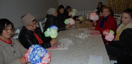Uczestniczki zajęć siedzą przy stole i trzymają w rękach wykonane przez siebie papierowe kwiaty w różnych kolorach.