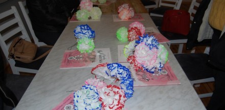 Kolorowe, papierowe kwiaty wykonane w ramach zajęć plastycznych leżą na stole.