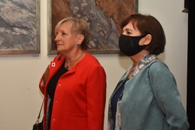 Dwie kobiety. Jedna z kobiet nosi maskę ochronną. W tle obraz.