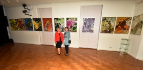 Dwie kobiety pozujące do zdjęcia na tle obrazów wiszących na ścianach.