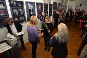 Wręczenie nagród laureatom konkursu- kobieta trzymająca czerwoną różę. W tle pozostali goście oraz wystawa zdjęć - Cyberfoto.