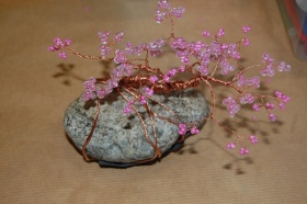 Kamień, który jest opleciony miedzianymi drucikami wraz z różowymi koralikami.