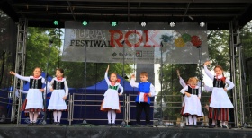 Para dzieci na scenie ubrana w stroje folklorystyczne trzymająca ręcę w górze