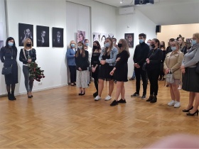 Grupa młodych osób ubrana w maseczki ochronne odwiedzający wystawę. Na ścianach wiszą fotografie.