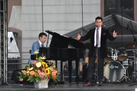 Występ muzyczny - na scenie śpiewający mężczyzna, w tle mężczyzna grający na fortepianie.