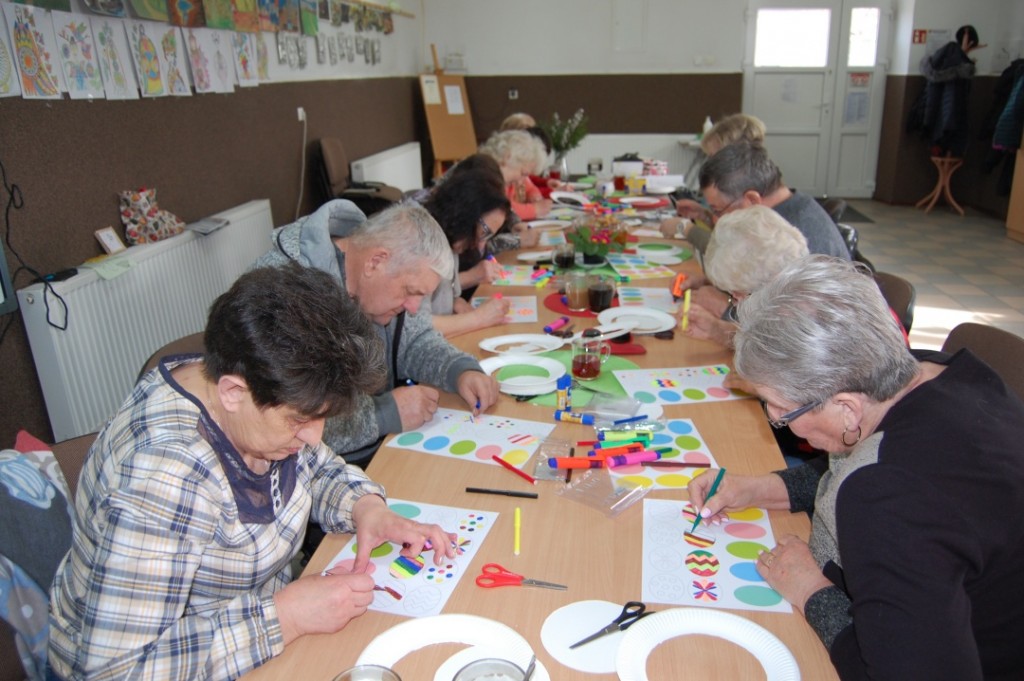 Zdjęcie stołu przy którym siedzą uczestnicy i wykonują prace plastyczne - kolorowe jajka wielkanocne.
